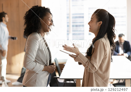 Young multiracial businesswomen colleagues laugh chat in modern office Young multiracial businesswomen colleagues laugh chat in modern office 129212497