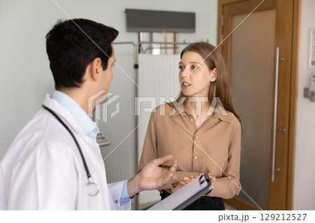 Serious young 20s patient woman talking to male doctor 129212527