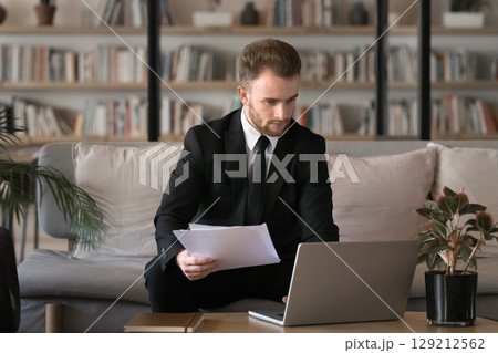 Businessman holding papers working on laptop in office 129212562