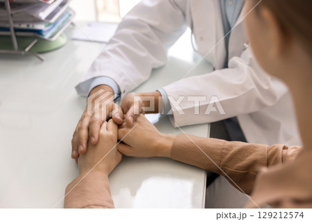 Young doctor man consoling patient, holding hands of woman Young doctor man consoling patient, holding hands of woman 129212574