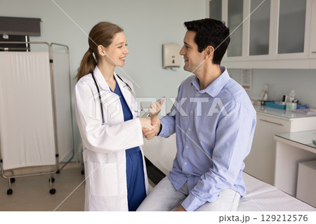 Cheerful young female doctor and male patient shaking hands 129212576