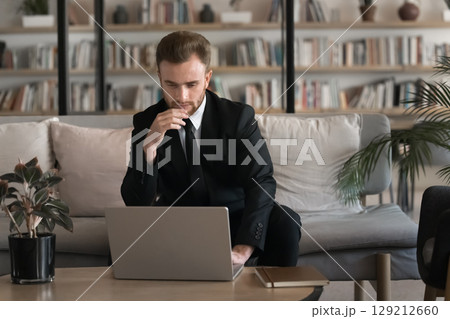 Serious European businessman in suit working on laptop in coworking Serious European businessman in suit working on laptop in coworking 129212660