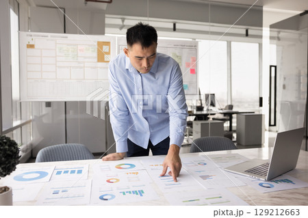 Focused Chinese professional man reviewing printed charts and graphs 129212663