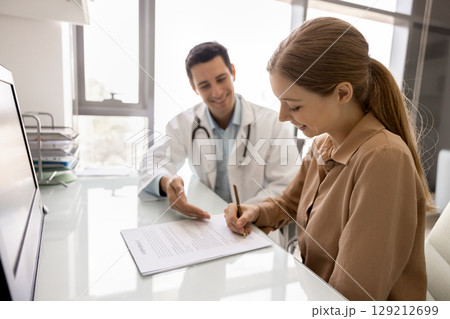 Positive male doctor pointing at contract for patient put signature Positive male doctor pointing at contract for patient put signature 129212699
