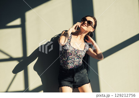 A young woman with a long ponytail stands against the wall, touching the screen of her phone 129212756