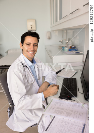 Happy handsome Latin practitioner man filling paper forms 129212794