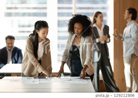Two young female colleagues review paper documents on office desk Two young female colleagues review paper documents on office desk 129212806