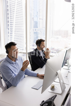 Men wearing headsets working at computers, engaging with clients remotely 129212810