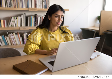 Focused Indian businesswoman working on laptop in workplace Focused Indian businesswoman working on laptop in workplace 129212837