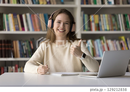 Female student in headphones sitting by notebook showing thumbs up 129212838
