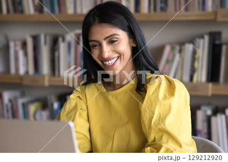 Cheery Indian woman reading pleasant news on laptop and laughing Cheery Indian woman reading pleasant news on laptop and laughing 129212920