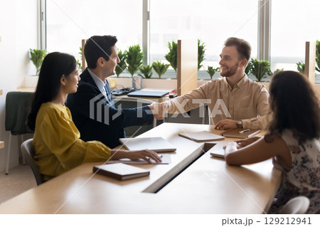 Businessmen shaking hands during formal meeting with teammates in office Businessmen shaking hands during formal meeting with teammates in office 129212941