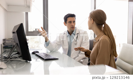 Serious male Latin physician explaining insurance terms to female patient Serious male Latin physician explaining insurance terms to female patient 129213146