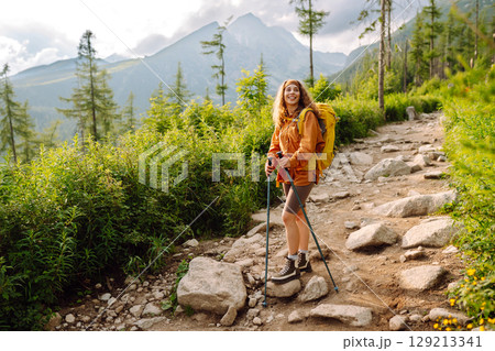 Young woman traveler hiking poles on trail among the mountains. Hiking. Active lifestyle. 129213341