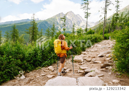 Young woman traveler hiking poles on trail among the mountains. Hiking. Active lifestyle. 129213342