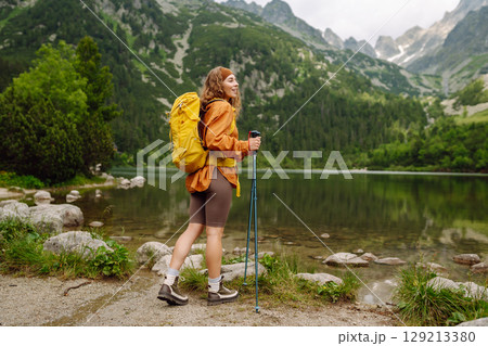 Female traveler with hiking backpack poses against backdrop of mountain lake. Adventure concept. 129213380