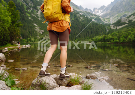 Female traveler with hiking backpack poses against backdrop of mountain lake. Adventure concept. Female traveler with hiking backpack poses against backdrop of mountain lake. Adventure concept. 129213408