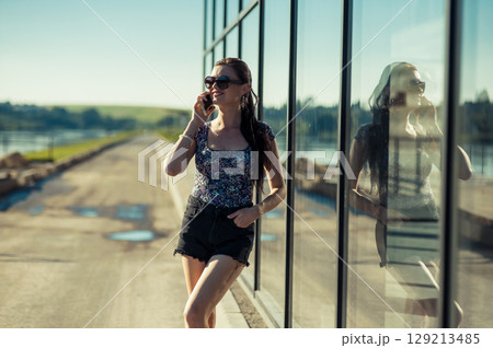 A young woman with a long ponytail and dark glasses is listening attentively to the caller at the glass facade A young woman with a long ponytail and dark glasses is listening attentively to the caller at the glass facade 129213485