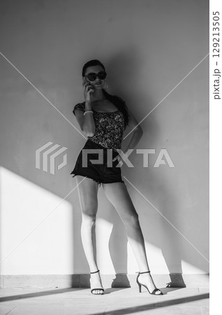 A charming girl is talking on the phone, leaning on the wall. 129213505