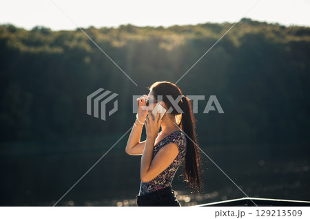 The young girl stands by the lake, holding her phone and smiling at a joke 129213509