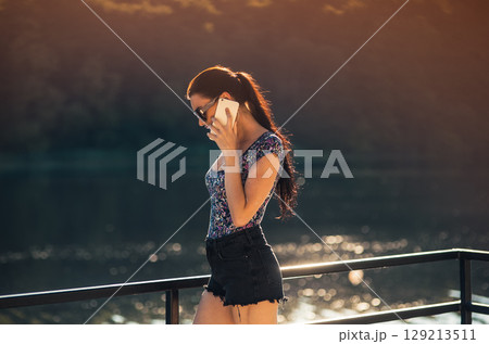 The girl in stylish sunglasses with a braided ponytail stands by the lake The girl in stylish sunglasses with a braided ponytail stands by the lake 129213511
