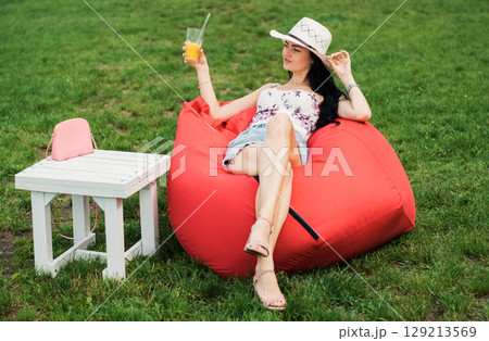 The girl in light summer clothing is nestled in a soft red chair by the lake 129213569