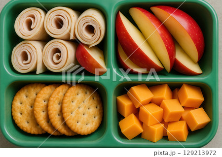 Healthy balanced lunchbox with rolled turkey slices, fresh apple wedges, cheddar cheese cubes, and whole grain crackers, AI Generative 129213972