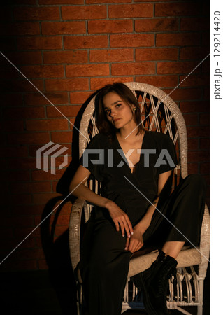 Fashionable woman in black suit in dark room on armchair 129214420