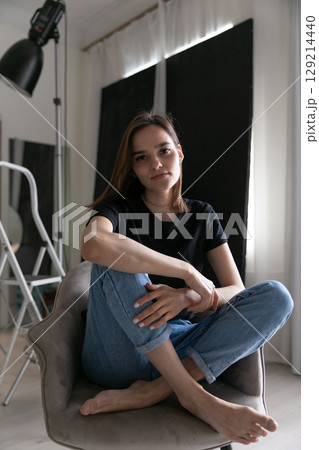 fashion brunette woman in jeans and t-shirt sitting on a chair 129214440