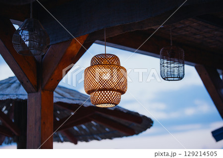 Wicker lamps under the roof of an open beach bar. Craft and handmade atmosphere. 129214505