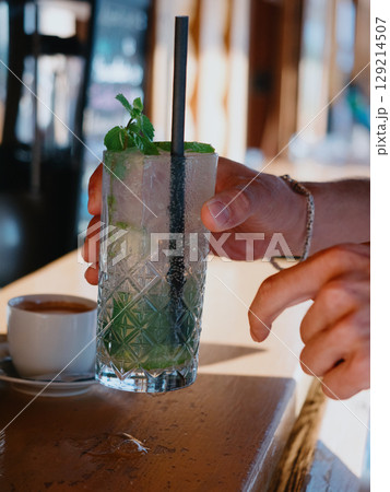 A customer at a beach bar picks up an ice-cold Mojito cocktail with paper straw 129214507