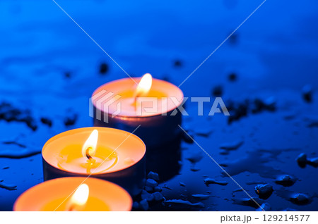 On a blue background, three small candles burn steadily and calmly 129214577