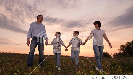 mother father children boy girl park sunset, man woman toddlers outdoors, Happy family walking in a field at sunset, Parents and children holding hands together, Family enjoying nature outdoors 129215262