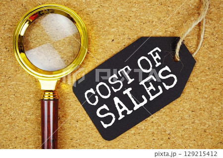 COS Cost Of Sales text on price tag with magnifying glass on cork board background COS Cost Of Sales text on price tag with magnifying glass on cork board background 129215412