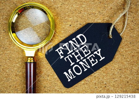 Find The Money text on price tag with magnifying glass on cork board background 129215438