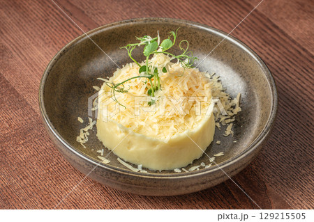Creamy mashed potatoes topped with grated cheese and microgreens in a rustic ceramic bowl 129215505