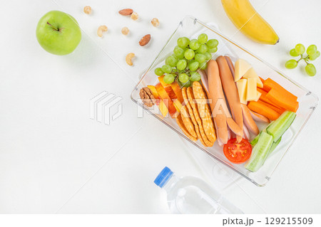 Balanced lunchbox with sausages, cheese, crackers, fruits, vegetables, and nuts on a white background. top view. copy space Balanced lunchbox with sausages, cheese, crackers, fruits, vegetables, and nuts on a white background. top view. copy space 129215509