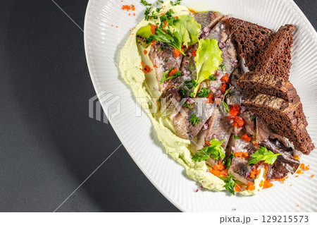 Pickled herring fillets served with creamy mousse, rye bread, red onions, herbs, and fish roe on a white plate. top view. copy space 129215573
