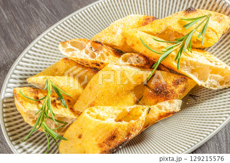Traditional Italian focaccia bread with golden crust and rosemary sprigs on a ceramic plate Traditional Italian focaccia bread with golden crust and rosemary sprigs on a ceramic plate 129215576