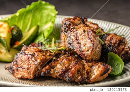 Grilled marinated pork pieces served with fresh greens and roasted zucchini on a ceramic plate 129215578