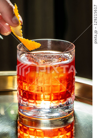 A classic cocktail served in a textured glass with a vibrant orange twist garnish, capturing a moment of refined elegance and refreshment. copy space A classic cocktail served in a textured glass with a vibrant orange twist garnish, capturing a moment of refined elegance and refreshment. copy space 129215617