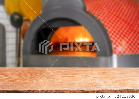 Empty wooden table in front of a traditional pizza oven with fire glowing inside 129215630