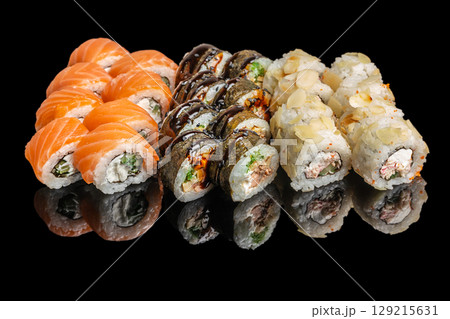 Assorted sushi rolls including salmon, seaweed, and almond-topped varieties arranged in rows on a glossy black background Assorted sushi rolls including salmon, seaweed, and almond-topped varieties arranged in rows on a glossy black background 129215631