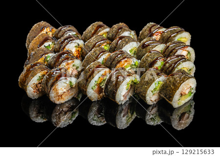 A large assortment of nori-wrapped sushi rolls filled with fish, vegetables, and drizzled with dark savory sauce, displayed on a glossy black surface A large assortment of nori-wrapped sushi rolls filled with fish, vegetables, and drizzled with dark savory sauce, displayed on a glossy black surface 129215633