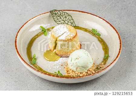 Matcha molten lava cake with a dusting of powdered sugar, paired with a scoop of pistachio ice cream and garnished with mint and crushed nuts on a decorative plate Matcha molten lava cake with a dusting of powdered sugar, paired with a scoop of pistachio ice cream and garnished with mint and crushed nuts on a decorative plate 129215653