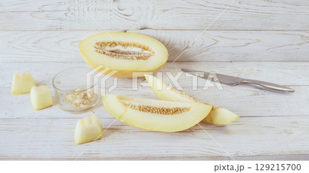 Cut ripe melon. Melon and knife on white wooden background. Top view. Beautiful still life. 129215700