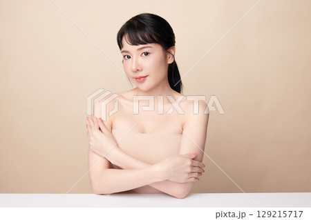 A beautiful young Asian woman with clean, fresh skin against a beige background. Skincare, facial treatment, cosmetology, beauty, and spa. An elegant portrait of an Asian woman. 129215717