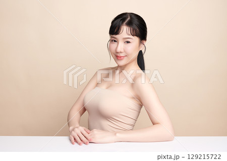 A beautiful young Asian woman with clean, fresh skin against a beige background. Skincare, facial treatment, cosmetology, beauty, and spa. An elegant portrait of an Asian woman. A beautiful young Asian woman with clean, fresh skin against a beige background. Skincare, facial treatment, cosmetology, beauty, and spa. An elegant portrait of an Asian woman. 129215722