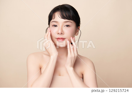 A beautiful young Asian woman with clean, fresh skin against a beige background. Skincare, facial treatment, cosmetology, beauty, and spa. An elegant portrait of an Asian woman. 129215724