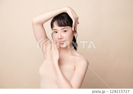 A beautiful young Asian woman with clean, fresh skin against a beige background. Skincare, facial treatment, cosmetology, beauty, and spa. An elegant portrait of an Asian woman. 129215727